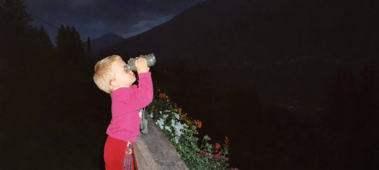 Kevin as a small child on a balcony at night, looking up at the sky through binoculars